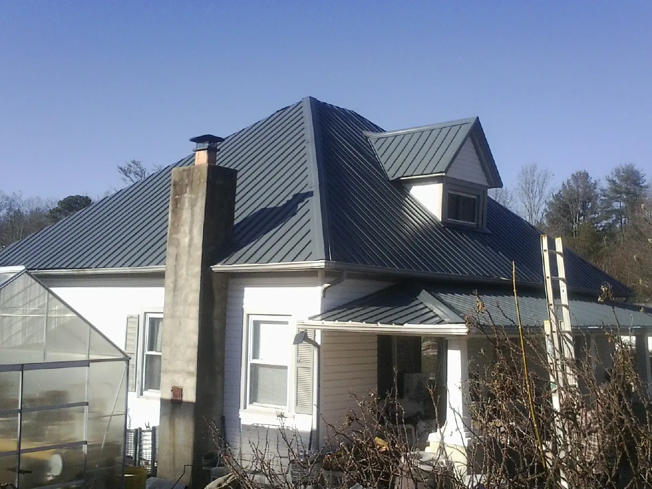 Dark blue standing seam metal roof on a white farmhouse with dormer — Slate & Tile Roof Repair by Roofing Brothers in Huger