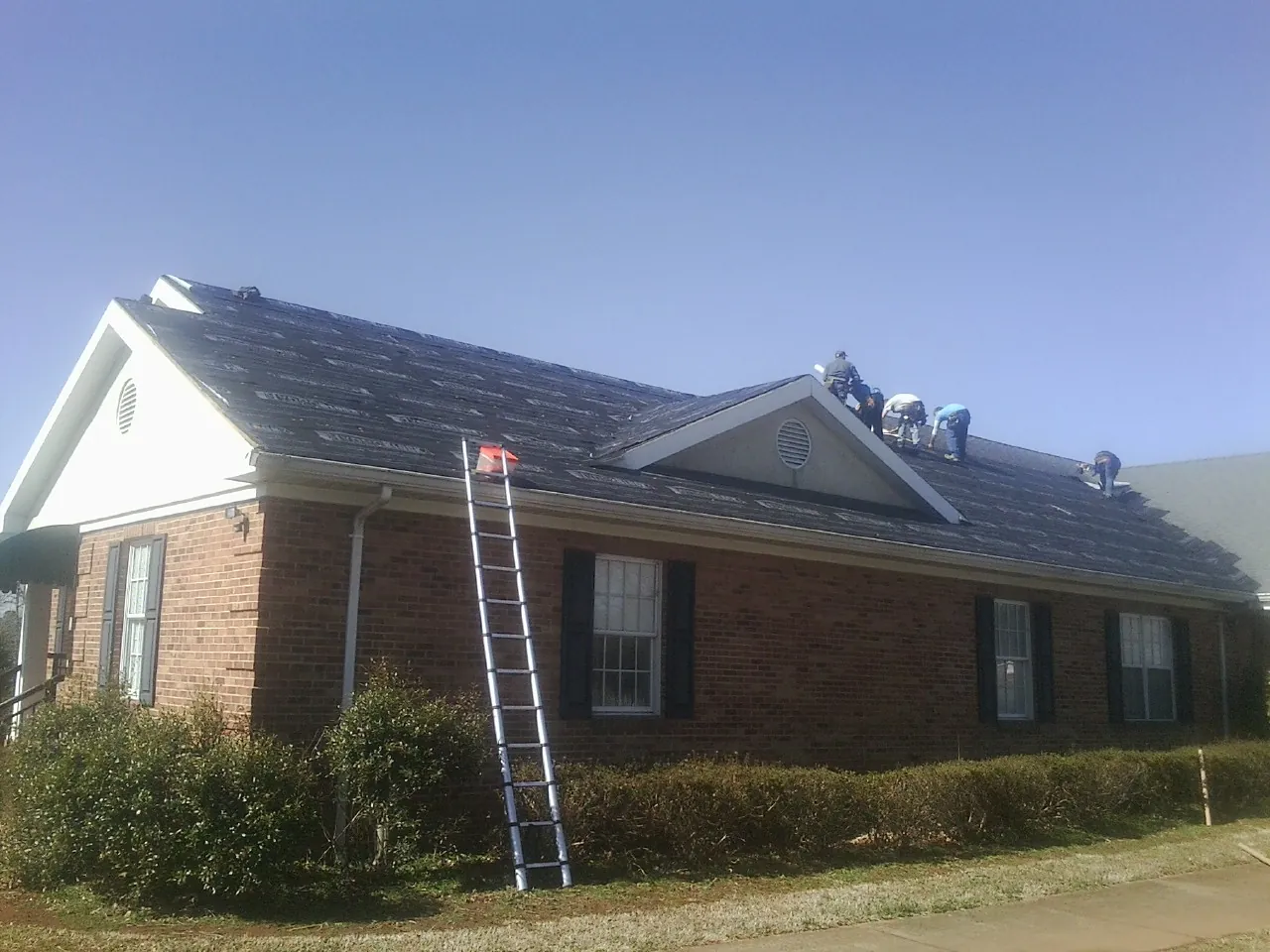 Crew tearing shingles off a brick ranch roof with a ladder set — Emergency Roof Repair work by our crew in Huger