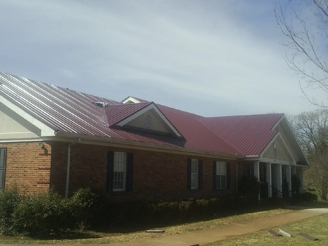 Red metal roof with gabled entries on a long brick building, from a Hail Damage Roof Repair job in Huger