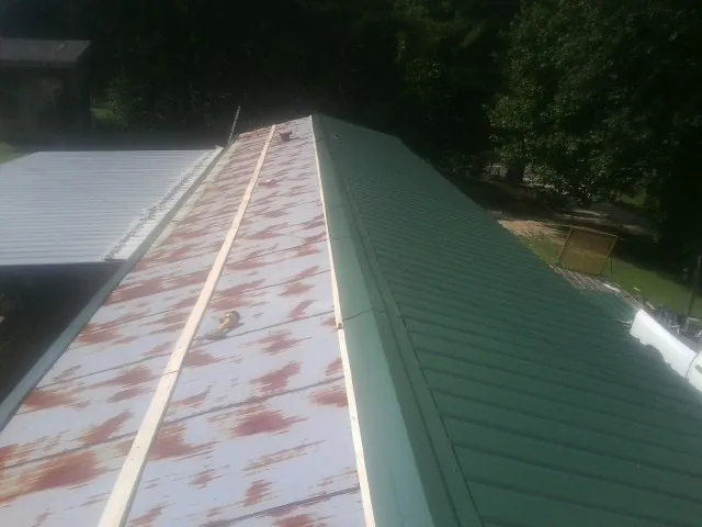 Old rusted panels beside newly installed green metal roofing — Wind Damage Roof Repair by Roofing Brothers in Huger
