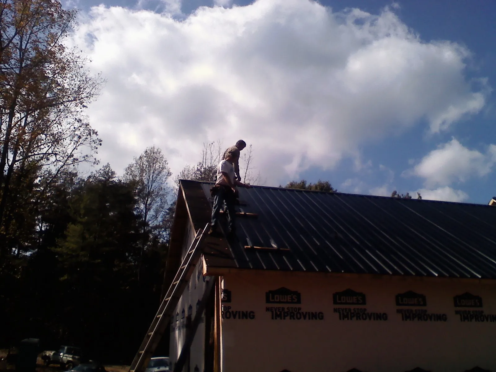 Roofer fastening dark metal panels high against a cloudy sky, from a Roof Inspection job in Huger