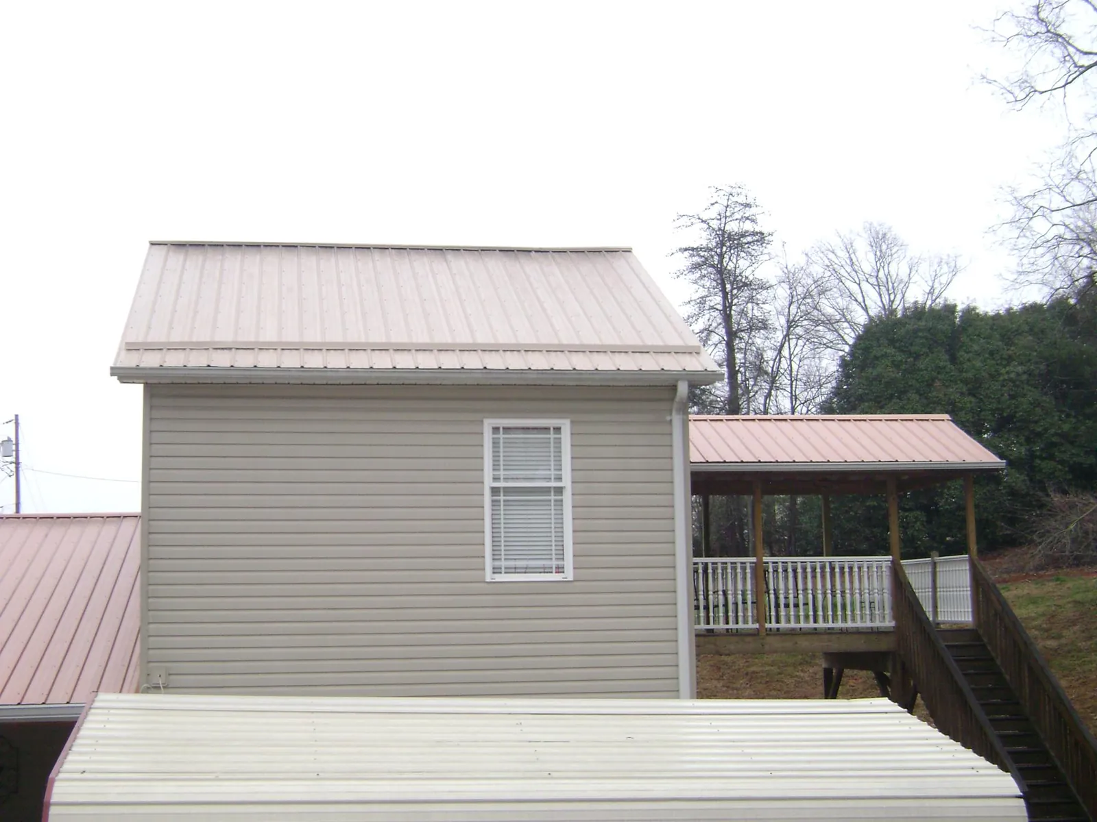 Tan metal roofs on a two story addition and attached porch, from a Roof Replacement job in Huger